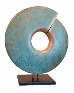 A circular, turquoise-green abstract sculpture—evoking the Infinite Circle Zen aesthetic—with a central hole and diagonal groove, mounted on a black rectangular base. The textured surface features patches of brown.